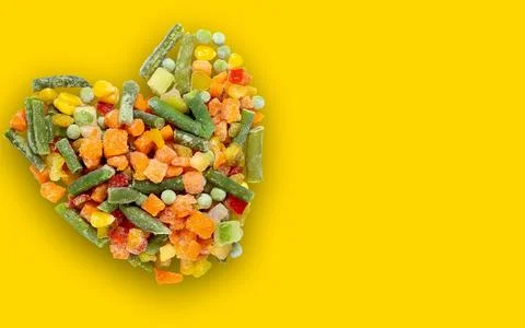 Frozen vegetable mixture in the shape of a heart with a shadow on a yellow ba Foto stock