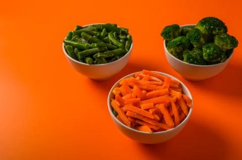 Frozen vegetables broccoli, spinach, carrot in bowls on an orange background Stock Photos