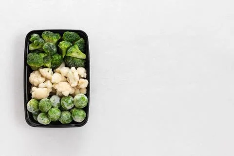 Frozen vegetables in a plastic container on a white background.  Stock Photos
