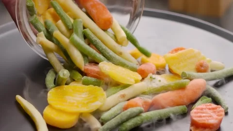 Frozen vegetables poured onto a sizzling hot pan closeup Stock-Footage 314111744
