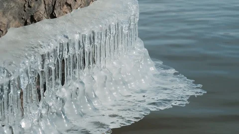 Frozen Water Icicles on Tree Stump above Water Stockbeeldmateriaal 104890843