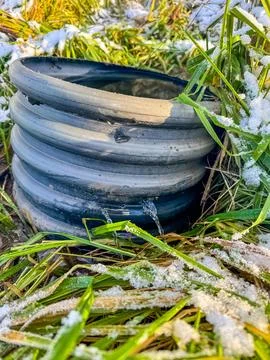 Frozen Water Pipe from which flows water with Snow and Grass in Winter Scene Stock Photos