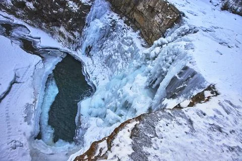 Frozen Waterfall and Turquoise Pool in Winter Snow at Rocky Cliff Edge Stock Photos