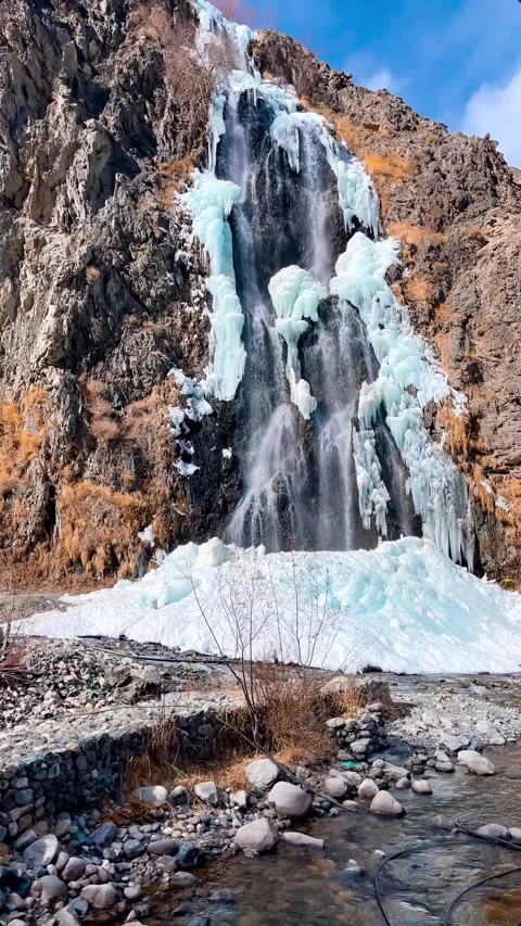 Frozen Waterfall Cascading Down Rugged Mountain with Icy Blue Chunks Stock Footage 329886706