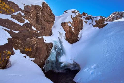 Frozen waterfall surrounded by snow on sunny day in Atlas mountains Stock Photos