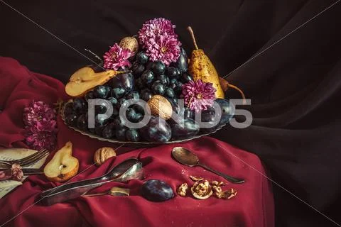 The fruit bowl with grapes and plums against a maroon tablecloth Stock Photos