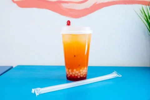 Fruit bubble tea in plastic cup on blue surface. Refreshing orange beverage Stock Photos