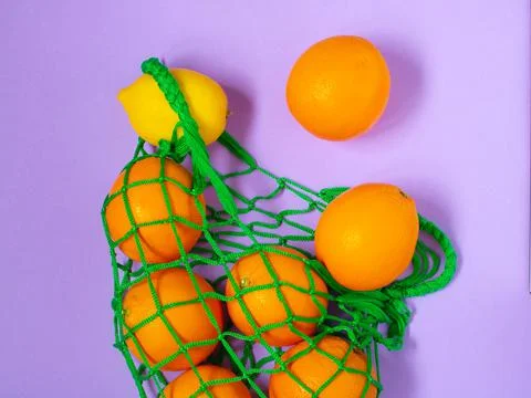 Fruit oranges and lemon lie on a colored background with a string bag. Stock Photos