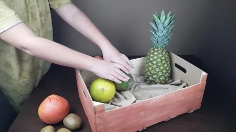 Fruit packaging wooden gift box. a man packs a gift of pineapple mango kiwi on a Stock Footage 173735340