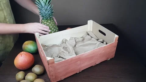 Fruit packaging wooden gift box. a man packs a gift of pineapple mango kiwi on a Stock Footage 201167589