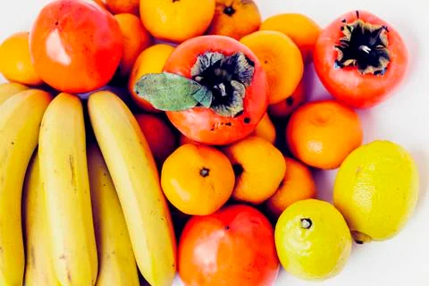Fruit plate on white background. Mandarins, bananas, persimmons and lemons. Stock Photos