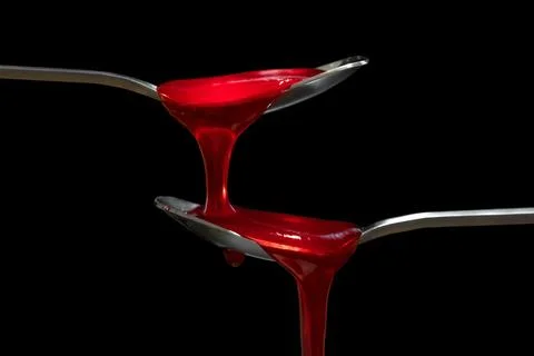 Fruit red jam dripping from spoon on black background Stock Photos