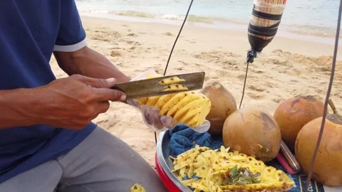 Fruit seller on the beach peeling pineapple, close-up Stock Footage 295484674
