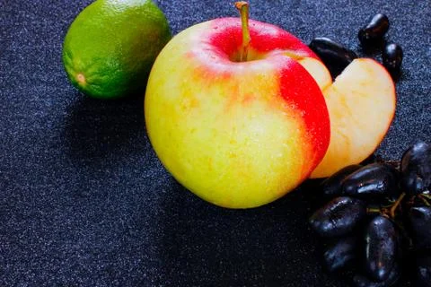 Fruit set. fresh lime, apple and grapes on a black surface. Stock Photos