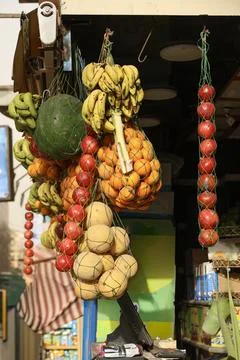 Fruit stand display with hanging net bags filled with bananas, oranges Stock Photos