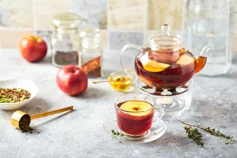 Fruit tea with apples and thyme in glass teapot and cup on the kitchen table Stock Photos