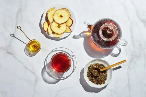 Fruit tea with apples and thyme and honey in glass teapot and cup on white Stock Photos