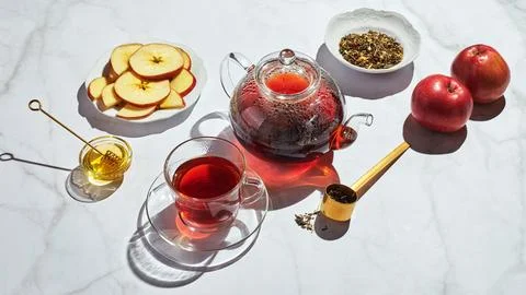 Fruit tea with apples and thyme and honey in glass teapot and cup on white ba Fotos Stock