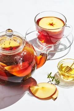Fruit tea with apples and thyme and honey in glass teapot and cup on white ba 写真素材