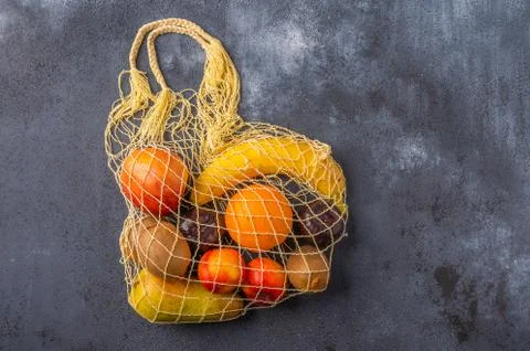 Fruits in the range in yellow eco string bag on a dark wooden surface Stock Photos