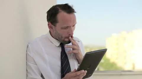 Frustrated businessman smoking a cigarette and looking at tablet computer HD Stock Footage