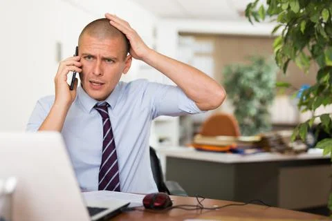 Frustrated businessman solving problems by phone in office Stockfoto's