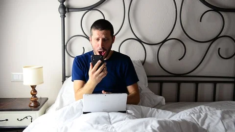 Frustrated businessman working on tablet while on bed he screams on smartphone 스톡 동영상 122306221