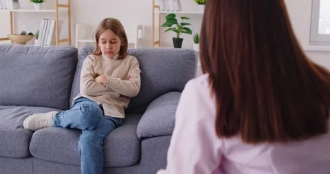 Frustrated child sitting on sofa, avoiding eye contact with psychologist during Stock Footage 330848595