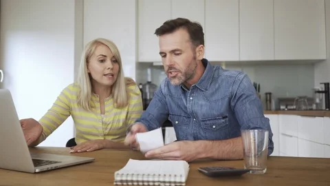Frustrated couple arguing while sitting in dining room with laptop and bills 動画素材 114605910