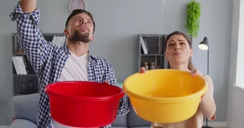 Frustrated Couple Under Umbrella Catching Ceiling Leak with Buckets in Apartment Video stock 321461209