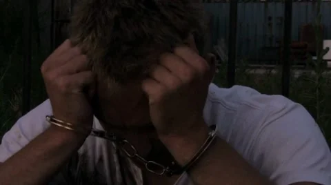 Frustrated kid arrested and in hand cuffs head in hands Stock Footage