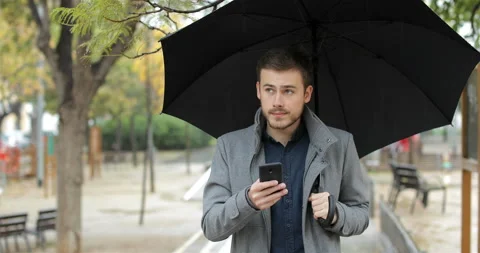 Frustrated man checking weather app on phone in a rainy day Stock Footage 99460515