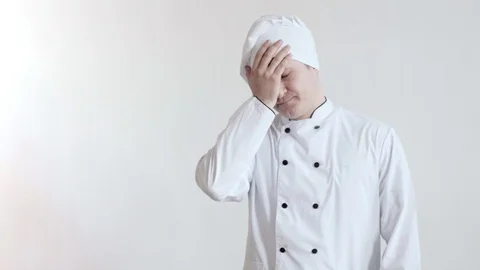 Frustrated man in chef's clothes does a facepalm, then grumbles and turns his Stock Footage 102718365