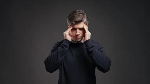 Frustrated man experiencing severe headache against grey studio background. Hand Stock Footage 341764665