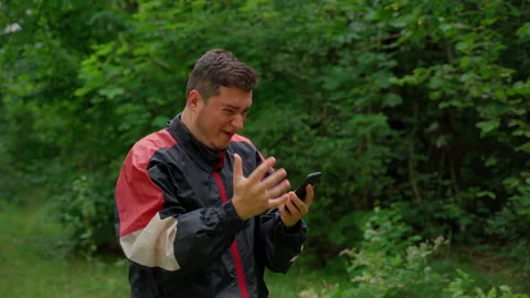 Frustrated man looking at smartphone gets angry in forest Stock Footage 158144004