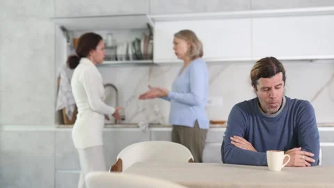 Frustrated man sitting in kitchen during quarrel between his wife and elderly 스톡 동영상 314243323
