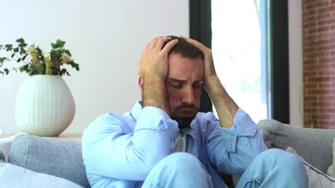 Frustrated man sitting on a sofa in his living room, suffering from a severe Stock Footage 344782149