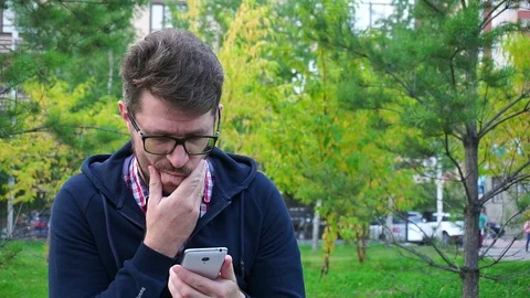 Frustrated middle-aged man sitting in the Park,writes messages in the smartphone 스톡 동영상 95160344