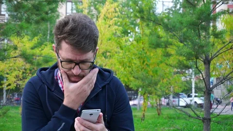 Frustrated middle-aged man sitting in the Park,writes messages in the smartphone Stockbeeldmateriaal 95160618