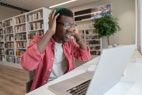 Frustrated student guy in library looking at laptop having tech problems during Stock Photos