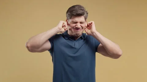 Frustrated young man covering ears to block unwanted noise. Stress, overload, co Stock Footage 340423979