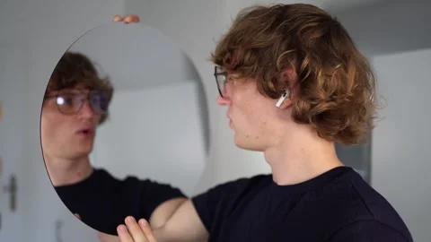 Frustrated young man gestures at his reflection in the mirror with a questioning Video stock 312981765