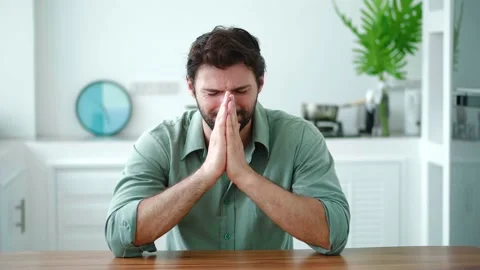 Frustrated young man sitting at the kitchen table in the home interior Stock Footage 213258910
