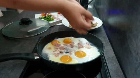 Fry eggs with bacon in a pan. Add spices. Breakfast is being prepared Stock Footage 204070630