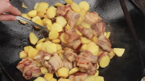 Fry potatoes with meat on a fire in a giant frying pan on a summer sunny day, cl Vidéo 136569925