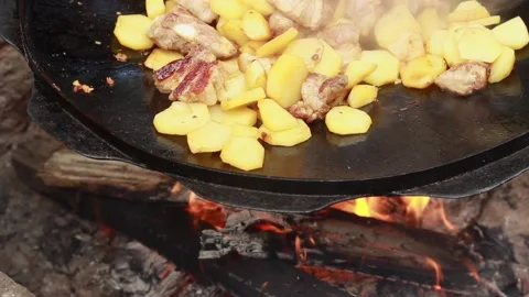 Fry potatoes with meat on a fire in a giant frying pan on a summer sunny day, cl Stock Footage 136570000