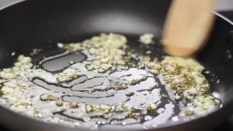 Frying and stirring of garlic and dried oregano in a frying pan with olive oil. Stock-Footage 154369972