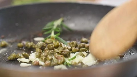 Frying and stirring of sliced garlic,capers and sprig of rosemary in a pan. Stock Footage 153482076