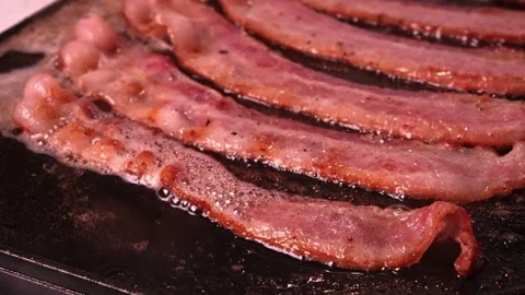 Frying bacon meat on the stove, close up view. Tasty Bacon strips being cooked. 스톡 동영상 334643026