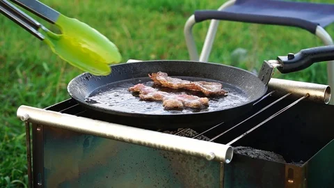 Frying bacon in a pan over charcoal during a picnic in nature. Stock Footage 125689991